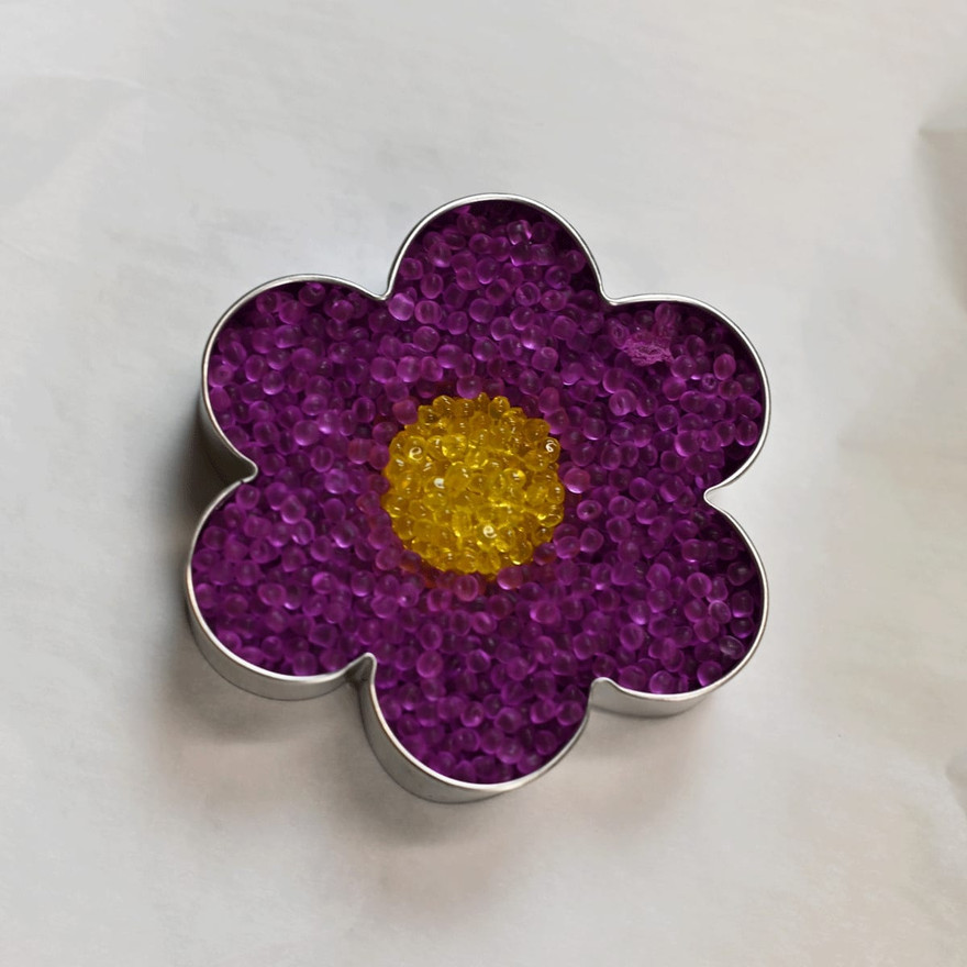 Flower cookie cutter filled with purple aroma bead petals around a yellow bead center