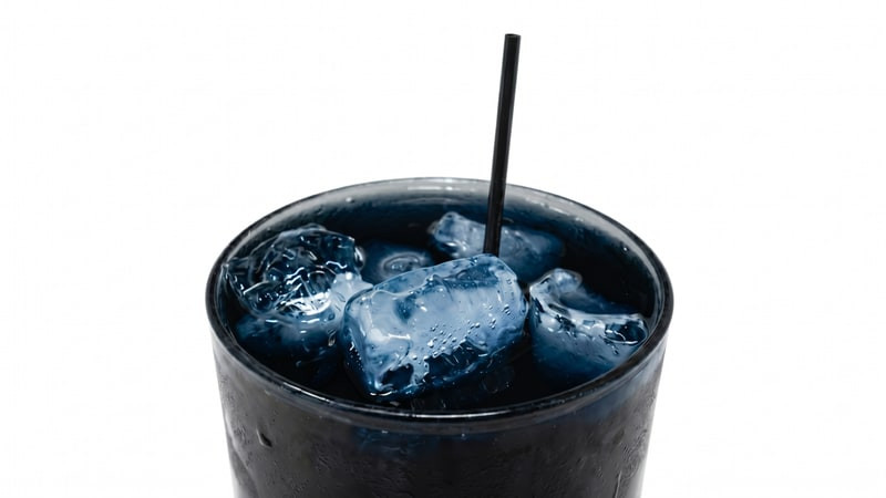 Dark blue iced drink with ice cubes and a black straw in a tumbler glass