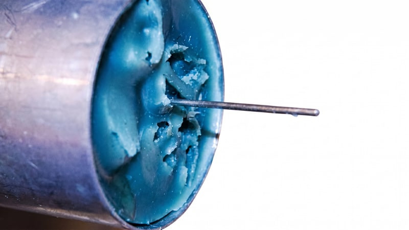 Close-up of a blue ice candle's pitted top with a metal wick pin inserted in the mold