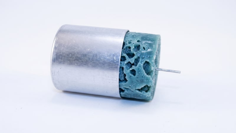 Teal-blue holey ice candle sliding out of an aluminum pillar mold lying on its side