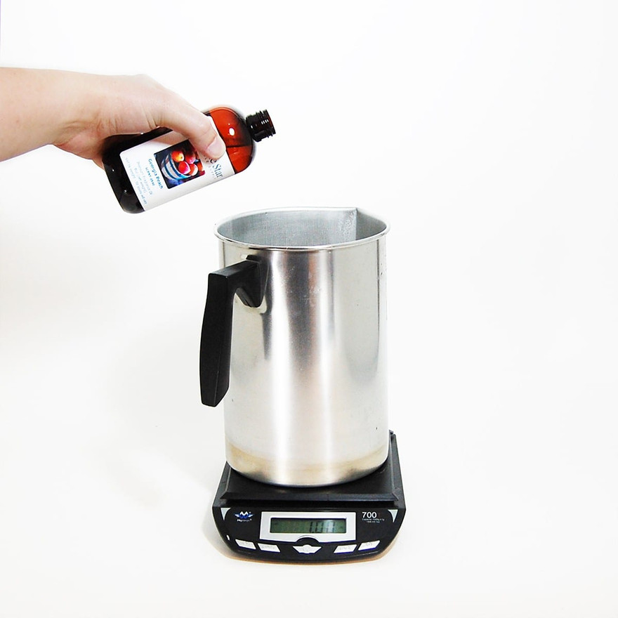 Hand tilting a Lone Star Georgia Peach fragrance oil bottle over an aluminum pitcher on a digital scale