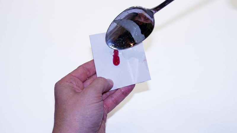 Spoon dripping melted red wax onto a white card held in one hand for a color test