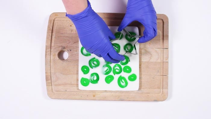 Blue-gloved hands pressing a star cutter into a white soap slab dotted with green spirals