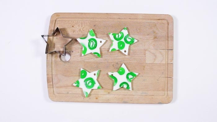 Four white star soaps with green swirls beside a metal star cookie cutter on a wooden board