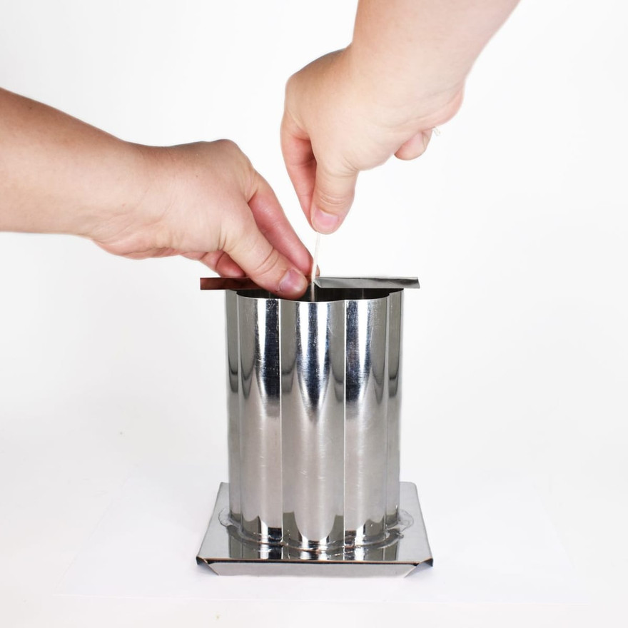Two hands threading a wick down into a fluted metal pillar mold on a paper plate