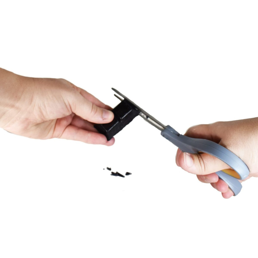 Hands using gray pliers to snip a piece from a black dye block, shavings below