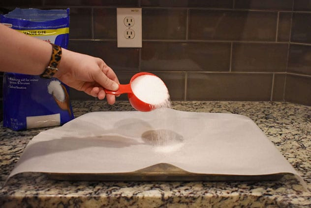 Hand pouring Epsom salt from a red measuring cup onto a parchment-lined baking sheet