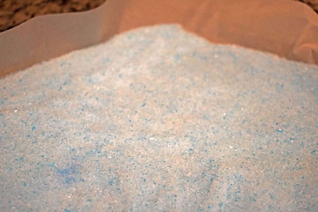 Mound of white bath salts flecked with blue grains on parchment paper