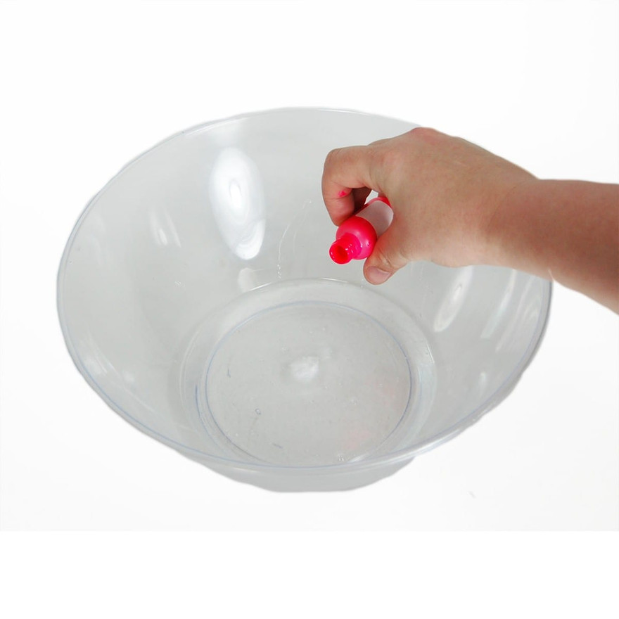 Hand squeezing a pink food-coloring bottle over an empty clear plastic mixing bowl