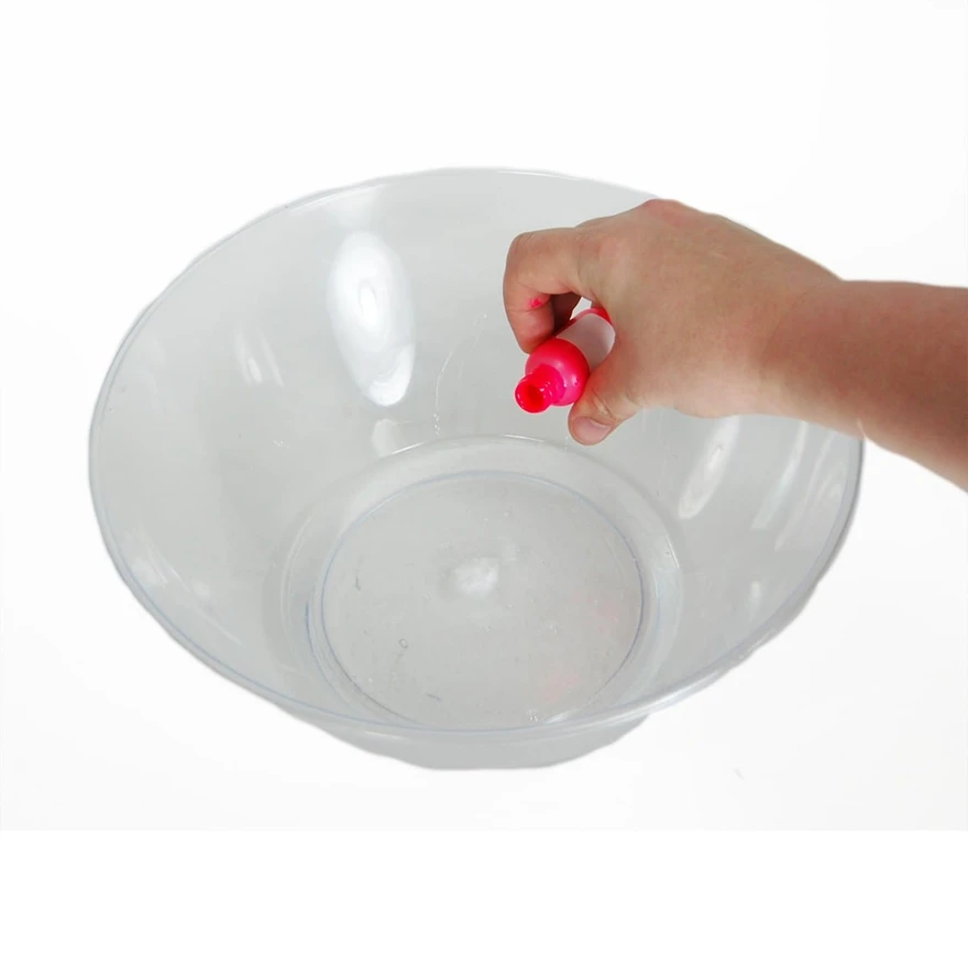 Hand squeezing a pink food-coloring bottle over an empty clear plastic mixing bowl