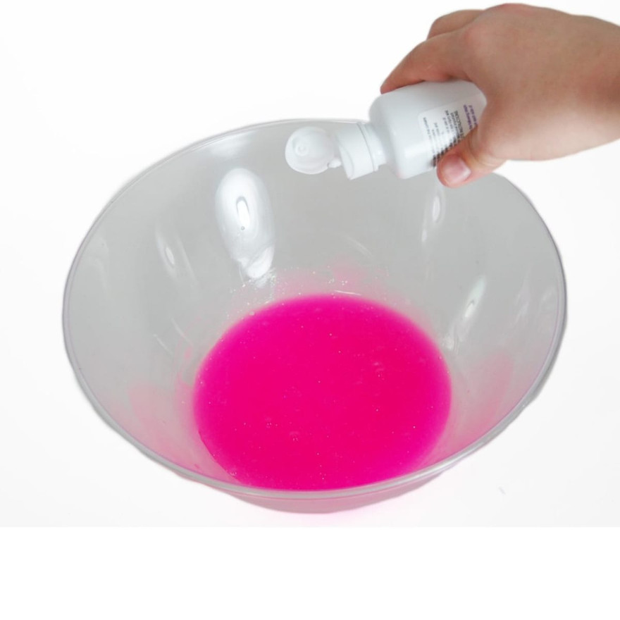 Hand tipping a white saline-solution bottle over hot-pink slime in a clear plastic bowl