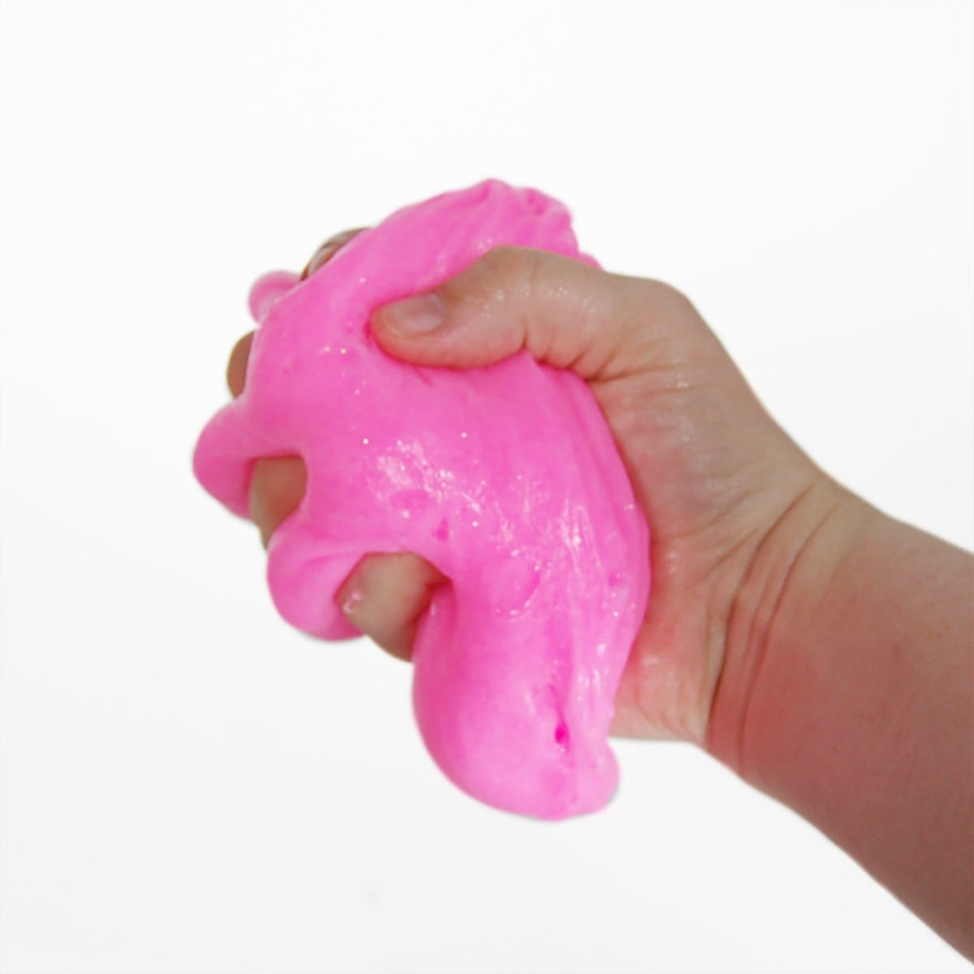Hand squeezing a glossy ball of bright pink stretchy slime against a white background