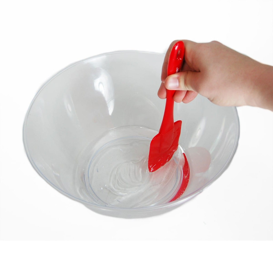 Hand stirring clear glue with a red spatula in a clear plastic mixing bowl