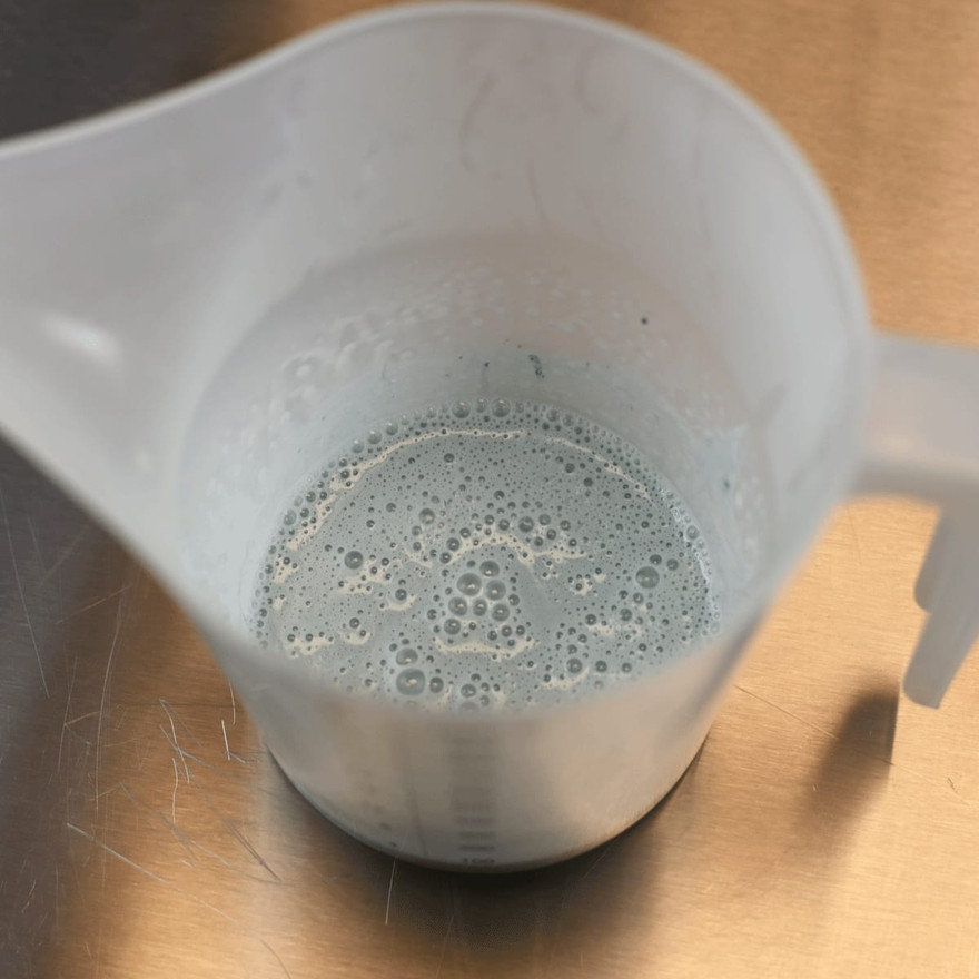 A pitcher of melted teal-tinted soap base with surface bubbles