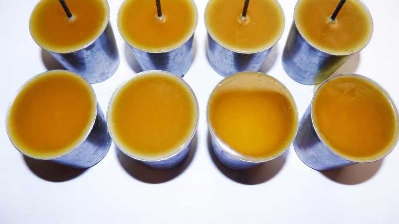 Overhead view of metal votive molds filled with orange wax around center wick pins