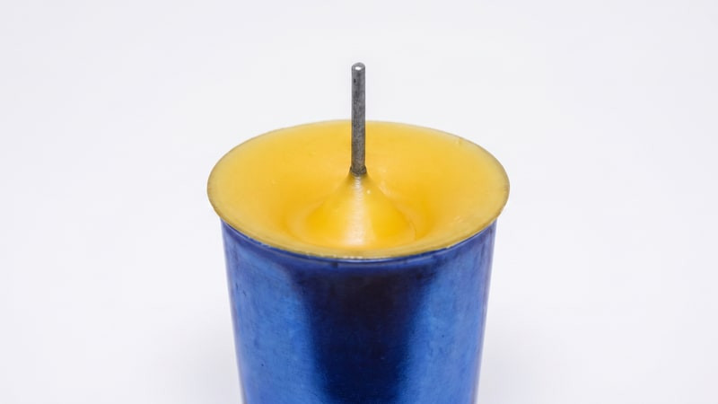 Single blue votive mold with yellow wax sunken into a well around the center wick pin