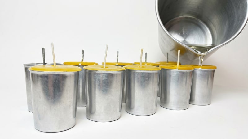 Topping off filled yellow votive molds with wax from an aluminum pouring pitcher