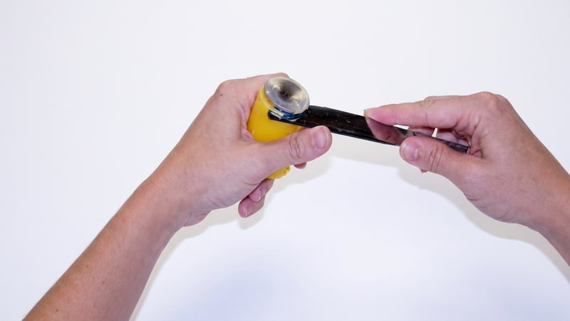 Hands pulling the wick pin from the base of a yellow votive candle