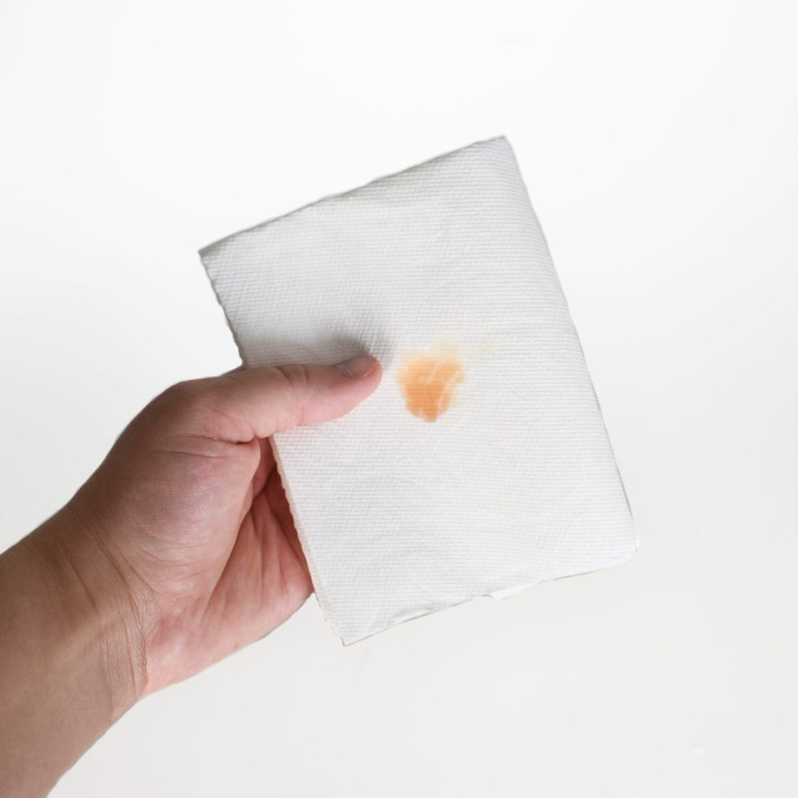 Hand holding a folded white paper towel with a small orange wax test spot
