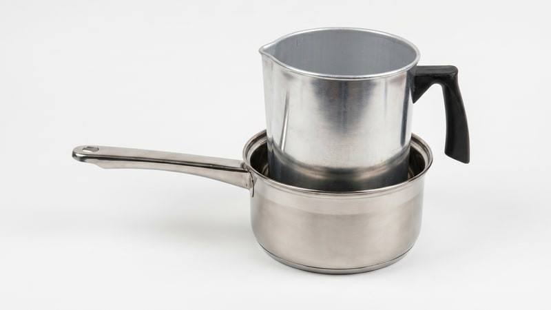 Aluminum pouring pitcher resting inside a stainless saucepan as a double boiler