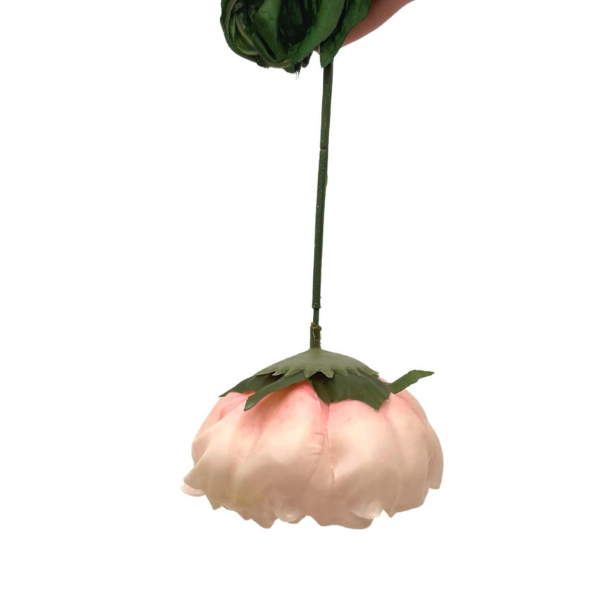 Wax-dipped pale pink faux peony hanging upside down by its green stem to dry