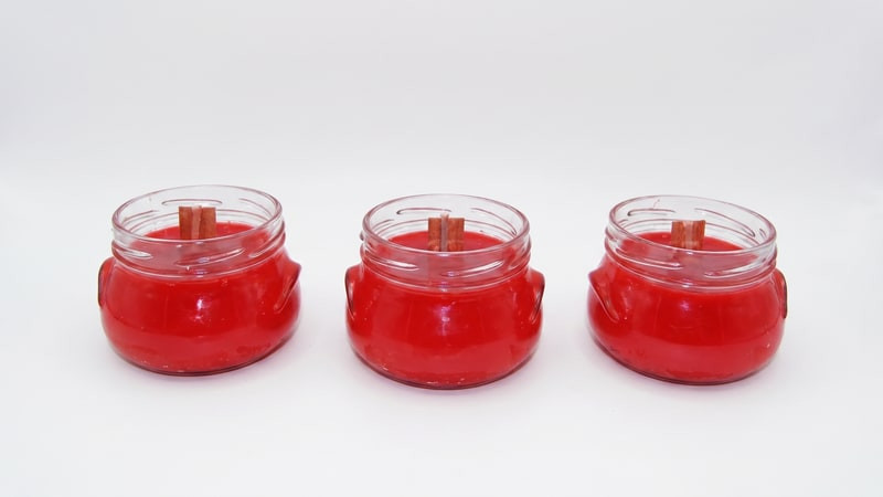 Three glass jars filled with bright red wax and centered wooden wicks cooling in a row