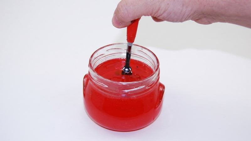 Hand dipping a red wax-coated tool into a bright red wax-filled glass jar