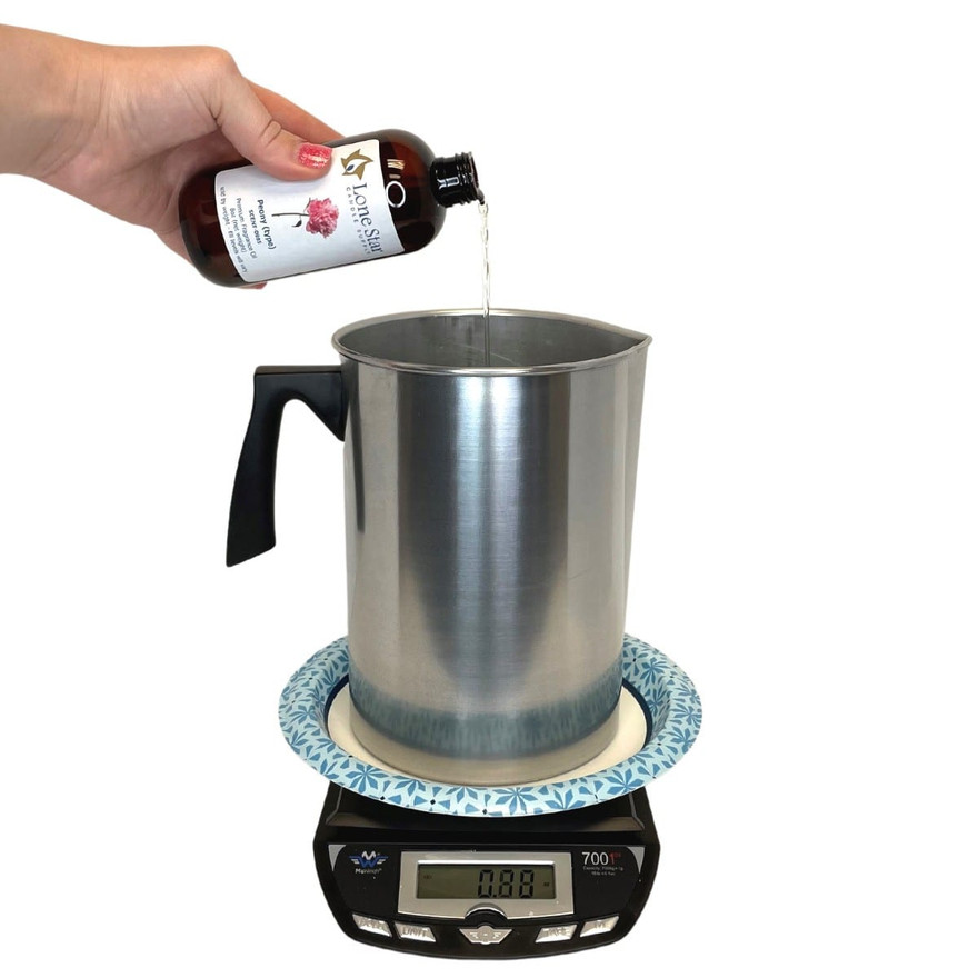 Hand pouring Lone Star Peony fragrance oil from an amber bottle into a metal pitcher on a digital scale