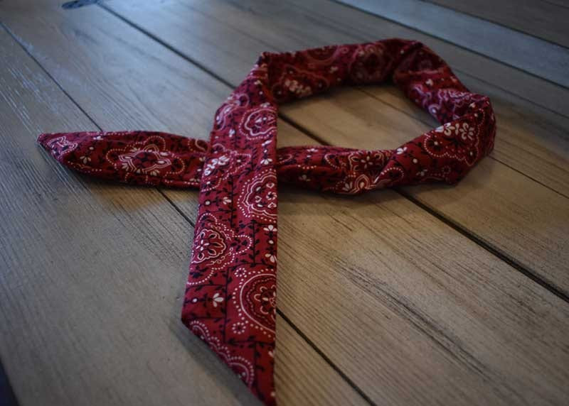 Finished red paisley bandana cooling neck wrap loosely coiled on a wood plank surface